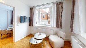 A modern living room with a sofa, a small table, a TV, and a window with curtains. - Apartment 9 | Boardinghouse Lüneburg No8A (Lüneburg)
