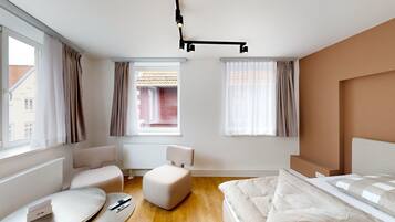 A modern bedroom with a bed, two chairs, a small ottoman, and a window with curtains.