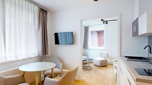 A modern hotel room with a dining area, a TV, a kitchenette, and a view of a brick wall. - Apartment 9 | Boardinghouse Lüneburg No8A (Lüneburg)