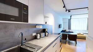 Een moderne keuken met een ingebouwde magnetron, een koffiezetapparaat en een broodrooster. Er is een klein zithoekje met een tafel en stoelen, en een bed met een raam op de achtergrond.