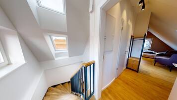 A modern loft bedroom with a wooden staircase, skylights, and a cozy reading nook.