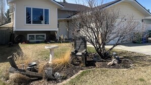 A single-story house with a front porch, a small garden with a birdbath, and a tree in the yard. - Bright, spacious 4 bedroom home. (Cochrane)