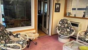 A cozy living room with wicker furniture, a glass door leading to a kitchen, and a framed picture on the wall. - Bright, spacious 4 bedroom home. (Cochrane)