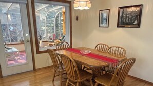 A dining area with a wooden table and chairs, a red runner, and a view through a glass door. - Bright, spacious 4 bedroom home. (Cochrane)