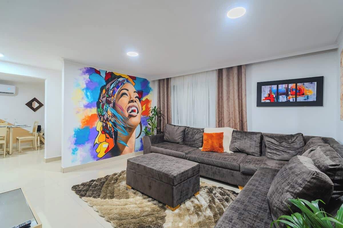 A modern living room with a large sofa, a coffee table, and a colorful mural on the wall.