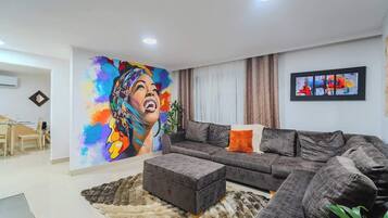 A modern living room with a large sofa, a coffee table, and a colorful mural on the wall.