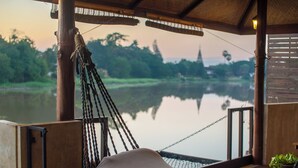 Un fauteuil suspendu en forme de hamac, offrant une vue sur un lac paisible et des arbres en arrière-plan.