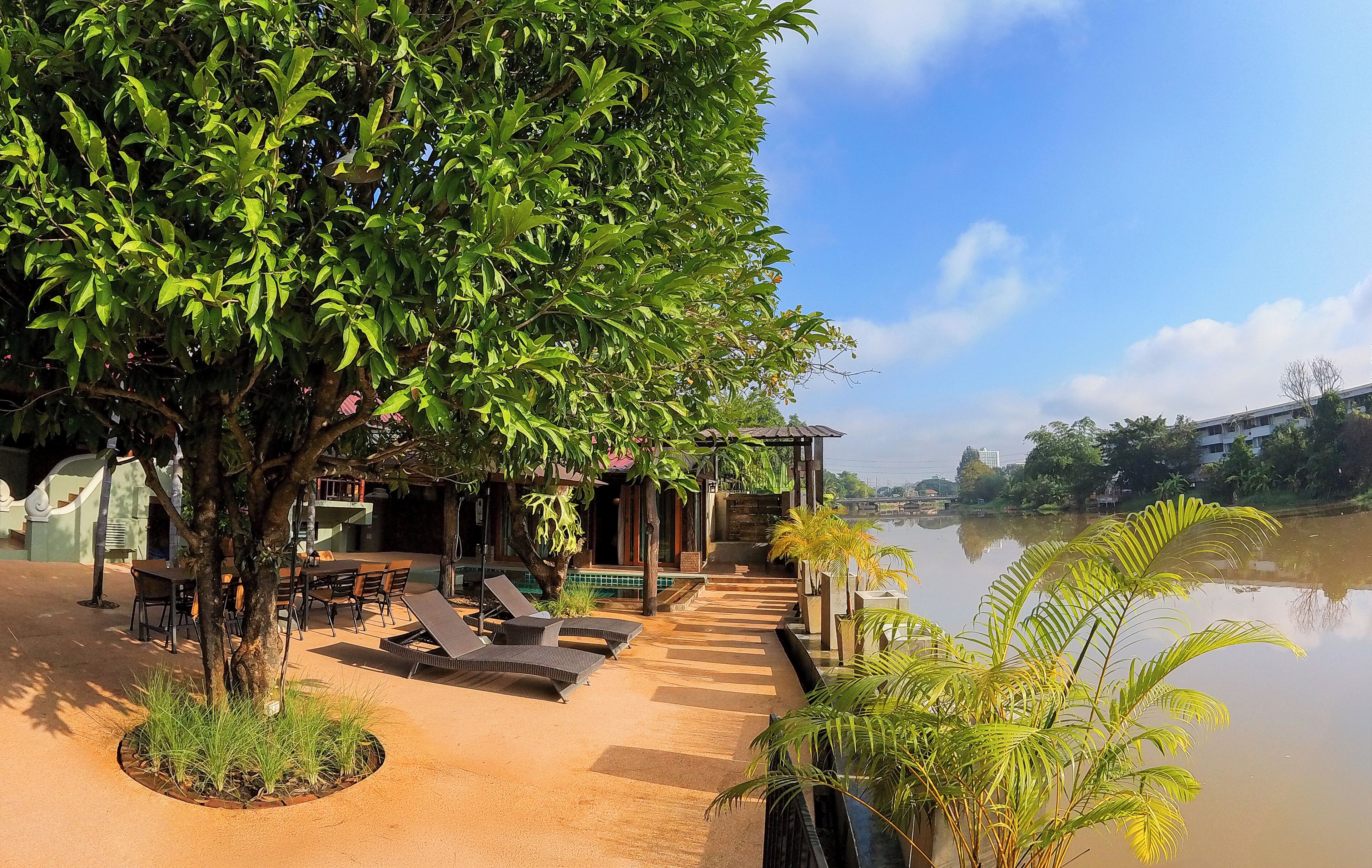 A serene outdoor seating area with a pool, surrounded by lush greenery and overlooking a calm body of water.