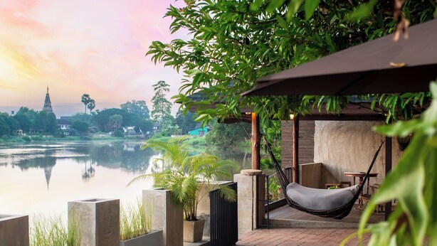 Un espace extérieur paisible, aménagé avec des sièges confortables, un hamac, des plantes en pot et offrant une vue sur un lac tranquille et un temple lointain.