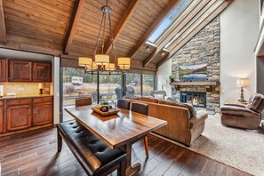 A spacious living area with a stone fireplace, wooden ceiling beams, and a large dining table. - Bright Breck Condo – Walk to Ski Lift & Shuttle (Breckenridge)