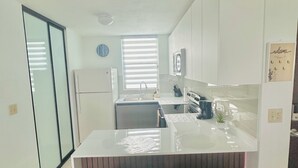 A modern kitchen with white cabinets, a large island, two yellow woven stools, and a clock on the wall.
