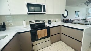A modern kitchen with white cabinets, a black stove, a microwave, and a coffee maker.