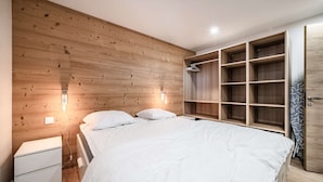 Un dormitorio con cabecera de madera, cama con ropa de cama blanca, mesita de noche, armario con varios estantes y vestidor.