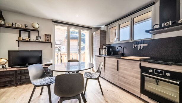 Una cocina moderna con comedor, armarios de madera, encimera negra y un ventanal grande.