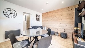 Un comedor moderno con una mesa redonda de vidrio, sillas negras con mantas de piel sintética, un panel de pared de madera y un reloj de pared.