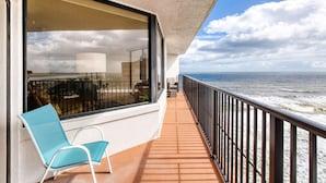 A balcony with a view of the ocean, a chair, and a railing.