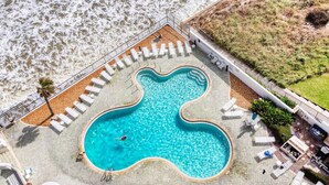 An aerial view of a swimming pool with a unique heart-shaped design, surrounded by lounge chairs and a small deck area.