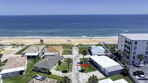 An aerial view of a coastal residential area with houses, a beach, and a large building with a flat roof. - Ocean Breeze Beach Bungalow (Ormond Beach)