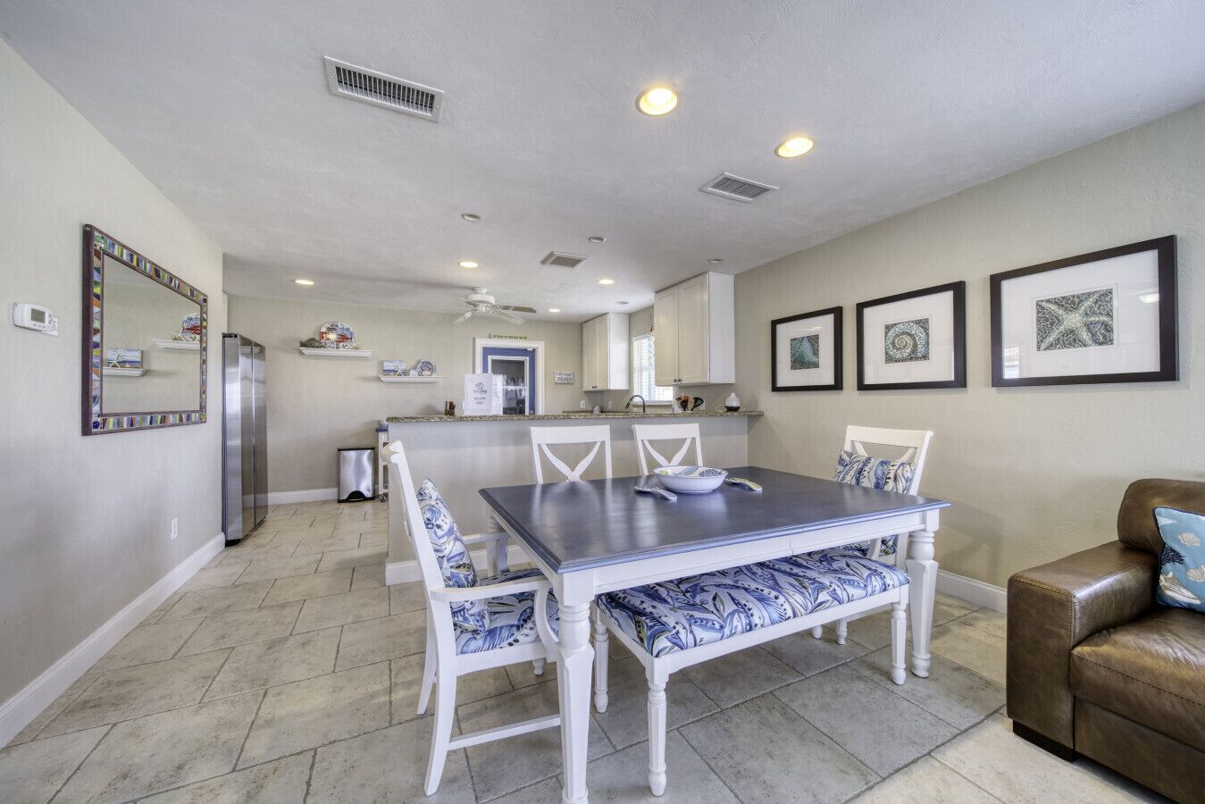 A dining area with a table and chairs, a refrigerator, and a kitchen in the background.