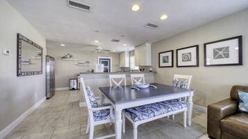A dining area with a table and chairs, a refrigerator, and a kitchen in the background.