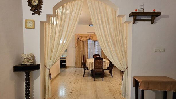 Un coin repas avec une table et des chaises, une horloge au mur et une arche surmontée d’un rideau.