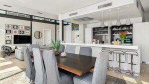 Una cocina moderna con una isla central, taburetes de bar y un comedor con sillas tapizadas en gris.