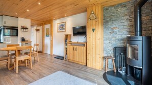 A cozy living room with a fireplace, wooden furniture, and a stone accent wall. - Epinettes : Vue montagne et déco contemporaine. (LE GRAND BORNAND)