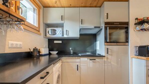 A modern kitchen with white cabinets, a microwave, an oven, and a washing machine. - Epinettes : Vue montagne et déco contemporaine. (LE GRAND BORNAND)