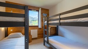 A bunk bed room with a wooden wall, a window with a view of mountains, and a radiator. - Réséda : Calme Montagnard avec Vue Apaisante (LE GRAND BORNAND)