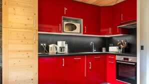 A modern kitchen with red cabinets, a microwave, a coffee maker, and an oven. - Réséda : Calme Montagnard avec Vue Apaisante (LE GRAND BORNAND)