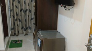 Une pièce de taille modeste équipée d’un réfrigérateur, d’un téléviseur à écran plat fixé au mur et d’une porte dotée d’une poignée.