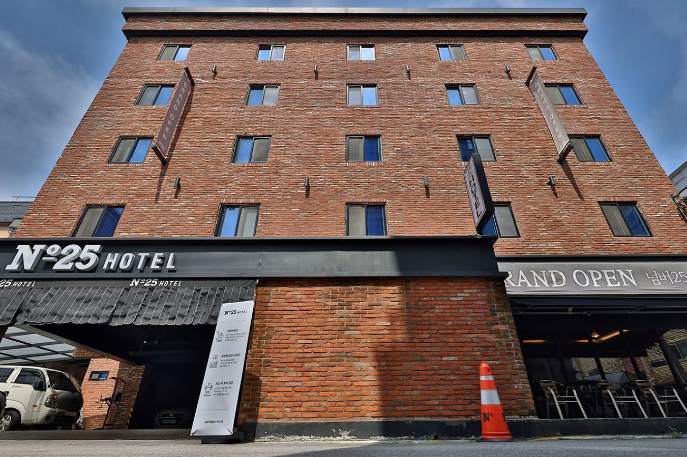 A brick building with a sign for "N°25 HOTEL" and a "Grand Open" sign.