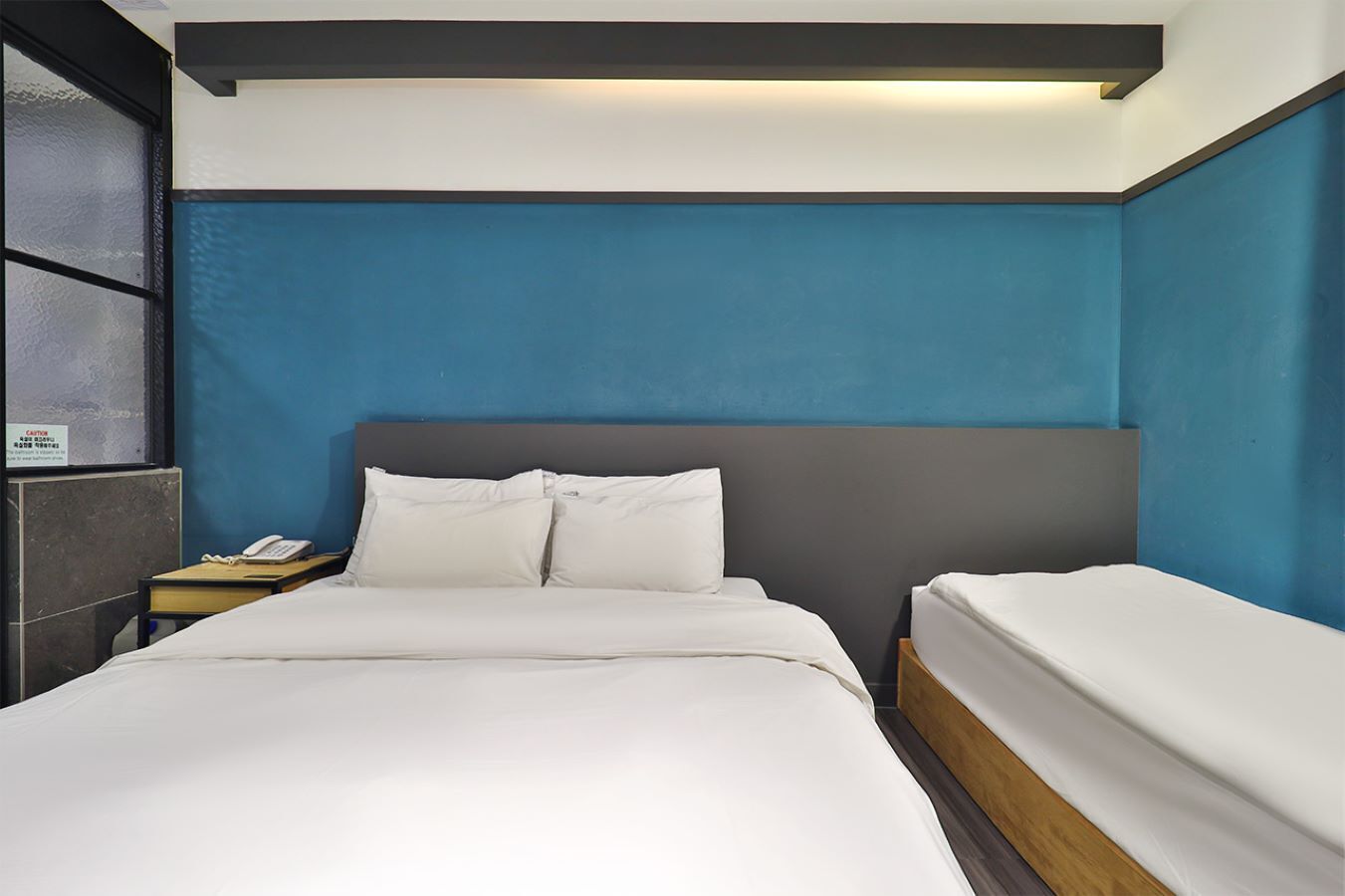 Una habitación de hotel con una cama grande, una mesita de noche con teléfono y una lámpara.