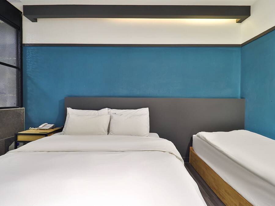 Una habitación de hotel con una cama grande, una mesita de noche con teléfono y una lámpara.