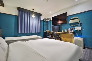 Hotellihuone, jossa on kaksi sänkyä, työpöytä tietokoneella, televisio ja peili.