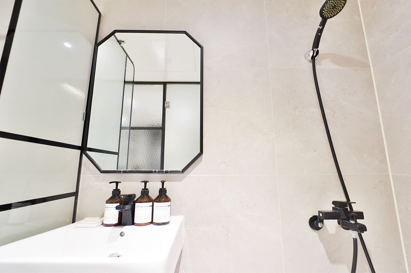 A bathroom with a white sink, a mirror with a geometric frame, and a handheld showerhead.
