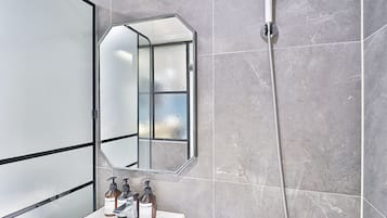 A bathroom with a glass-enclosed shower, a mirror, and a sink with soap dispensers.