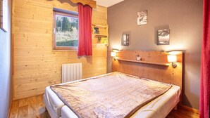 A wooden room with a bed, a window with a red curtain, a radiator, and wall-mounted shelves with books. - Nice apt 4 pers near the slopes (Chamrousse)