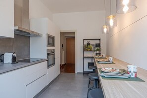 A modern kitchen with a built-in oven, a coffee machine, and a dining area with a table set for two. - Urban Oasis - My Home in Como (Como)