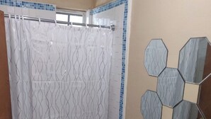 A bathroom with a shower curtain, a toilet, a sink, and decorative hexagonal mirrors. - Charming family friendly home,furnished with parking facilities,near malls/beach (Nassau)