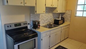 A compact kitchen with white cabinets, a stove, a sink, and a microwave. - Charming family friendly home,furnished with parking facilities,near malls/beach (Nassau)