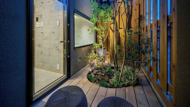 Une terrasse extérieure moderne, dotée d’un pont en bois, d’un petit jardin et d’une porte vitrée donnant sur une pièce.