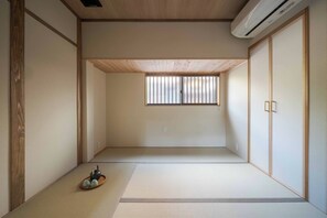 A traditional Japanese room with tatami flooring, sliding doors, and a window with vertical blinds. - Tokisora Machiya Holiday House     (Kanazawa)