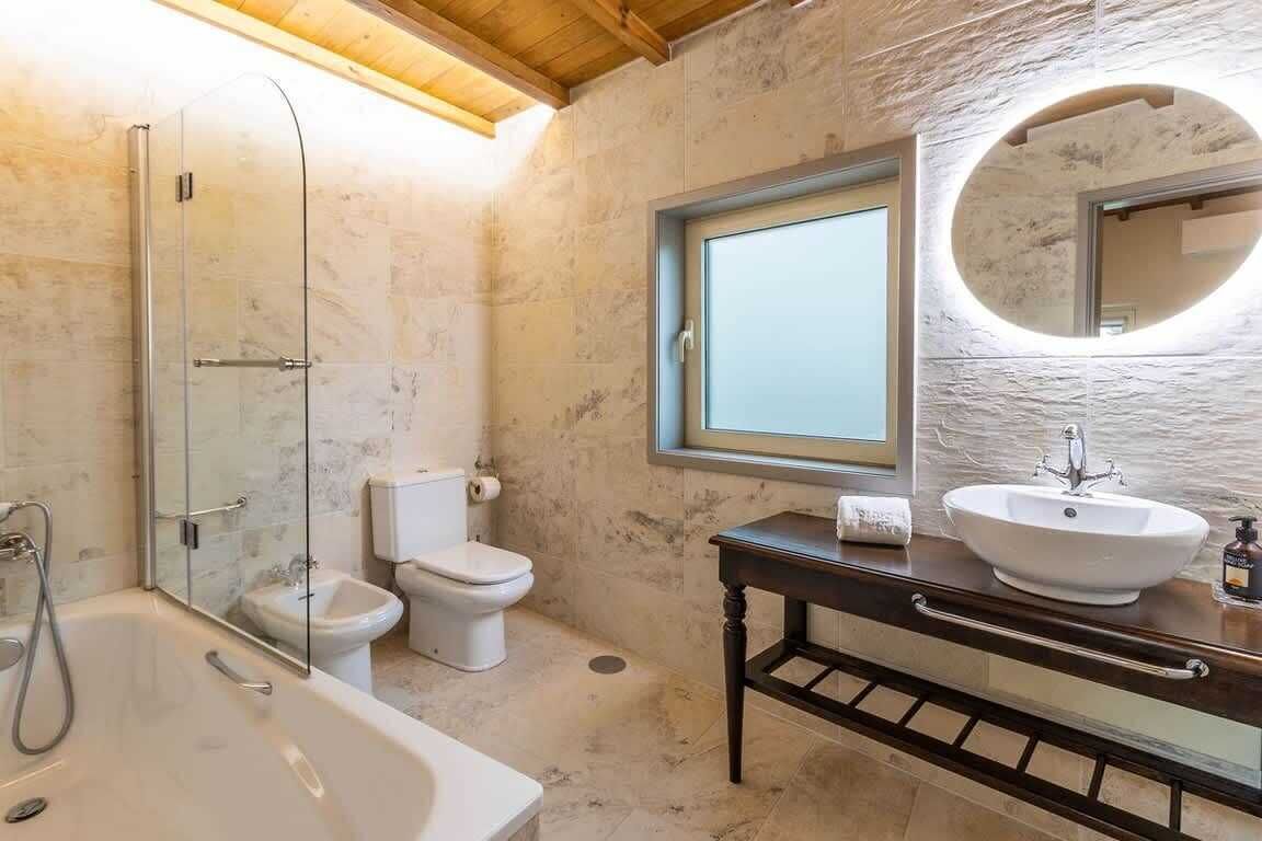 Een badkamer met een douchecabine, een wit toilet, een wastafel met spiegel en een houten wastafelmeubel.