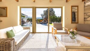 Ampla sala de estar com uma grande porta de vidro deslizante que dá para uma piscina ao ar livre, mobiliário de vime e uma mesa de centro de mármore.