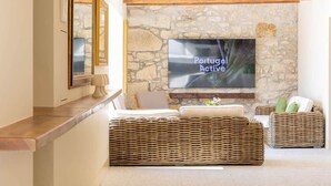 Sala de estar com parede de pedra, televisão de tela plana, móveis de vime e teto de madeira.