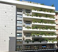 A modern building with multiple balconies, each adorned with green plants.