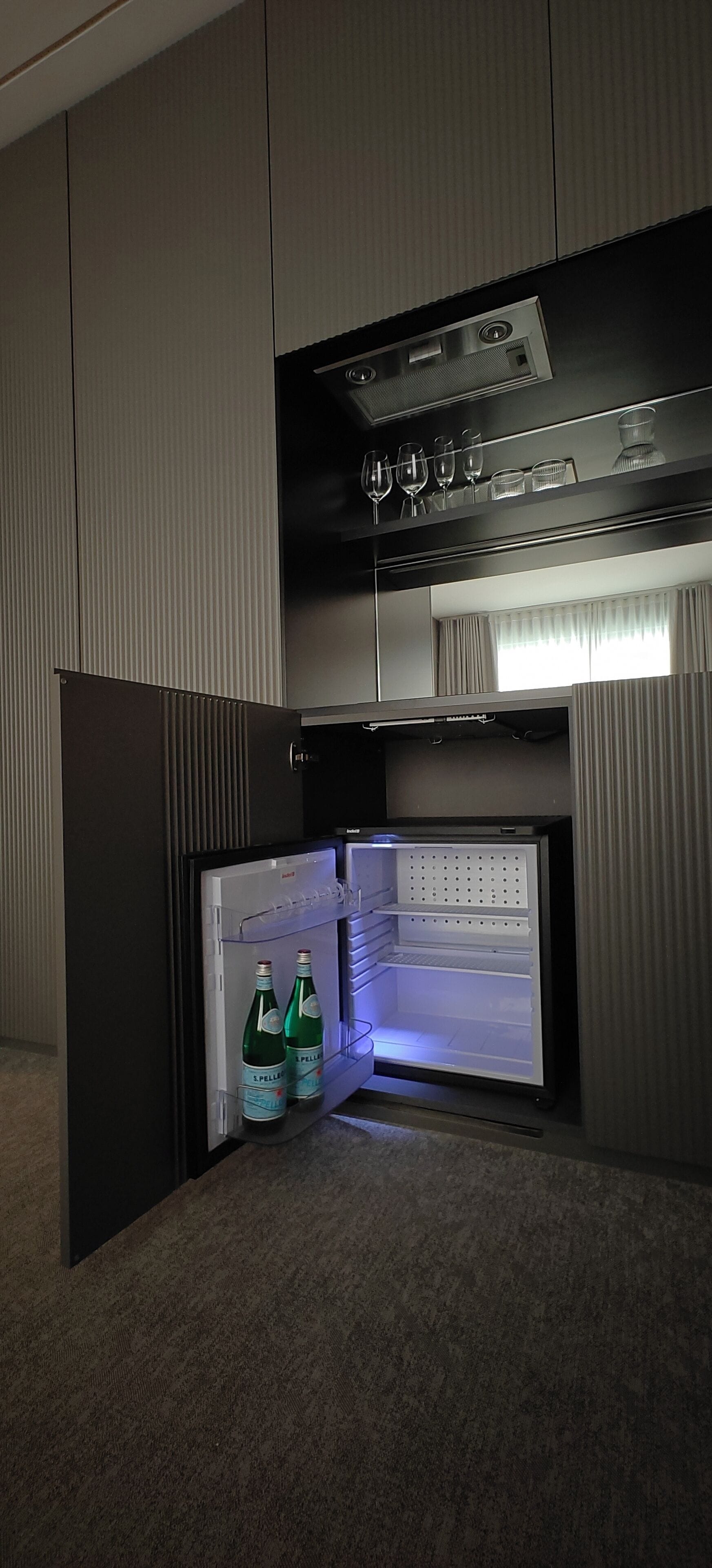 A compact refrigerator with two bottles of L'PELLER wine, a wine glass, and a wine glass holder on top.