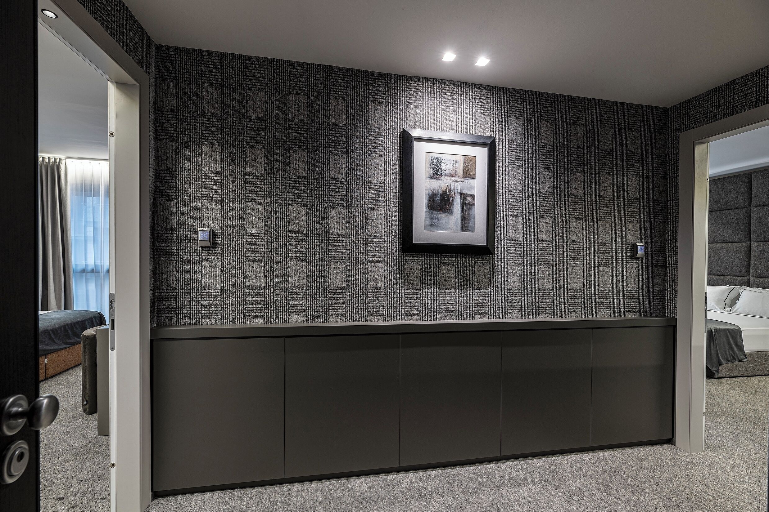 Een moderne hotelkamer met een donkere receptiebalie, een ingelijst kunstwerk aan de muur, en een bed dat in de aangrenzende kamer zichtbaar is.