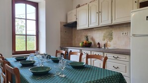 Een eethoek met een tafel voor vier personen, een raam met uitzicht op groen, en witte kasten boven het aanrecht.